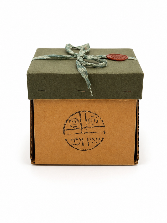 Caja de regalo con tapa verde, cinta de tela y sello de lacre con el símbolo de Misticarium